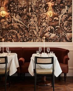 two tables with white tablecloths and candles in front of an ornate wallpaper