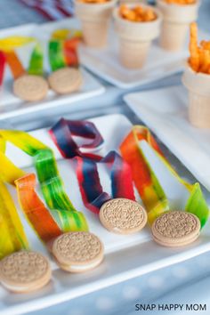 some snacks are sitting on trays next to cups and plates with candy in them