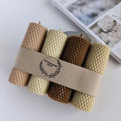 four rolled up candles sitting on top of a white table next to a book and magazine