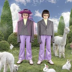 two children in purple pants standing next to llamas and alpacas on the grass