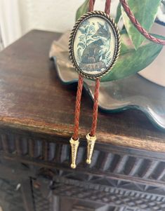 This awesome bolo tie has a vintage fox print with a clear resin coating and metal backing. Handmade in our shop!The cord is brown and made of genuine woven leather.Our bolos pair nicely with many of our belt buckles! They make wonderful gifts.The western bolo tie rope length is 39'' ; pendant size is 1 1/2'' x 1 1/4'' Vintage Adjustable Hand Tooled Bolo Tie, Adjustable Vintage Hand Tooled Bolo Tie, Brown Concho Bolo Tie Lariat, Western Brown Bolo Tie With Concho, Western Brown Bolo Ties With Concho, Brown Concho Bolo Ties Lariat, Brown Concho Bolo Tie, Vintage Bolo Tie With Adjustable Length For Western Events, Vintage Bolo Ties With Adjustable Length For Western-themed Events