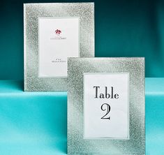 two silver glittered frames with a table number