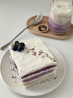 a piece of cake with white frosting and blueberries sits on a plate next to a glass of milk