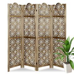 an ornate wooden room divider next to a potted plant on a white background