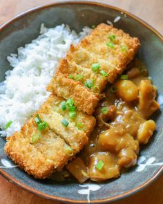 a bowl filled with rice, meat and gravy on top of a wooden table