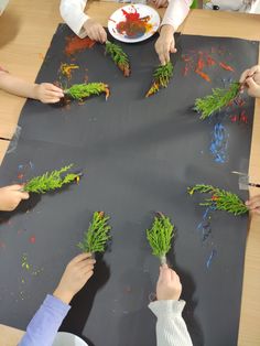 several children are doing arts and crafts with green plants on a black paper sheet that is laid out in the shape of a circle