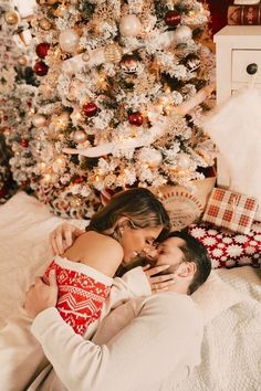 a man and woman laying in front of a christmas tree