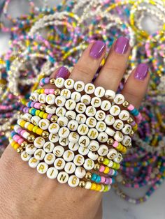 a woman's hand holding a bracelet with letters on it and beads all around her