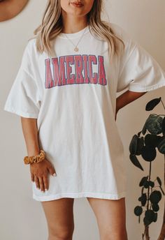 AMERICA - USA FLAG - LIGHTWEIGHT TSHIRT IN WHITE This graphic tee is soft and cozy with a loose fit that you will want to live in! A perfect shirt for all the patriots who love America, land of the free. AMERICA on the front, with a distressed USA vintage flag on the back. It is flattering on both men and women and can be the perfect oversized tee when you order up a size or two! * Q U I C K * F A C TS * - Graphic is a high quality digital print which is durable and long lasting. - Comfort Color Usa Graphic Tee, White Summer T-shirt For College, Summer Game Day T-shirt With Text Print, Summer College Style T-shirt With Letter Print, Summer Streetwear T-shirt With School Spirit, Summer College Style T-shirt With Graphic Print, Spring Varsity T-shirt With Graphic Print, White T-shirt With American Flag Print For Spring, Spring Cotton Varsity T-shirt