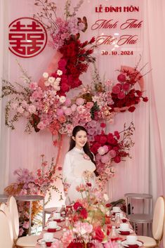 a woman standing in front of a table with flowers on it and plates around her