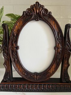 an ornate wooden frame on a shelf with a potted plant in the back ground