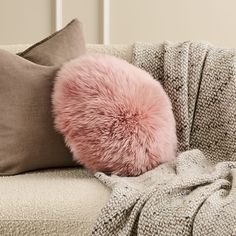 a pink fluffy ball sitting on top of a couch next to two throw pillows and a blanket