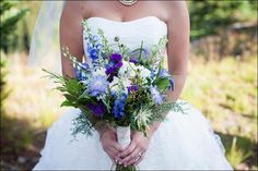 a woman in a wedding dress holding a bouquet of blue and white flowers on her hand