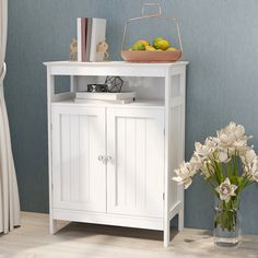 a white cabinet sitting next to a vase with flowers and fruit on top of it