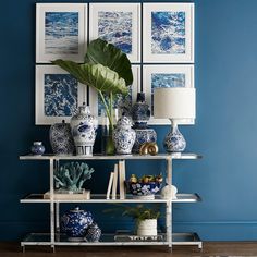 blue and white vases on a shelf in front of pictures with green plant next to them