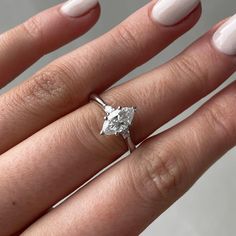 a woman's hand with a diamond ring on her finger and white manicured nails