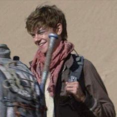 a smiling man holding a baseball bat in his right hand and wearing a scarf around his neck