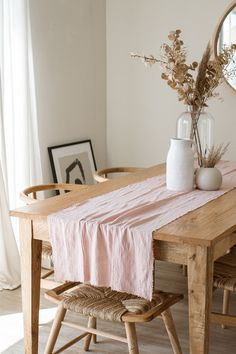 a wooden table topped with a vase filled with flowers next to a mirror and chair