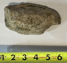 a piece of rock sitting on top of a white table next to a measuring tape