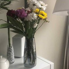 two vases filled with flowers on top of a white table next to a lamp