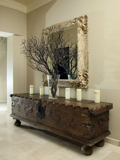 a wooden trunk with candles on it in front of a mirror and vases filled with branches