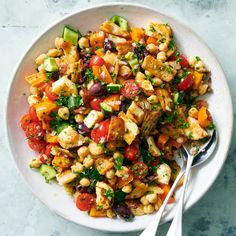 a white bowl filled with chickpeas, tomatoes, cucumbers and other veggies