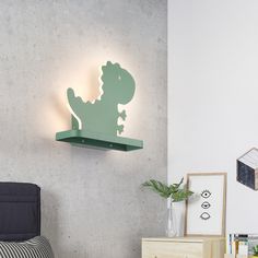 a green dinosaur light mounted on the wall above a bed in a room with white walls