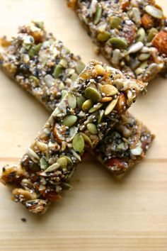 three pieces of granola bar sitting on top of a wooden cutting board with nuts and seeds