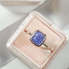 a ring with a blue stone is sitting in a pink box on a white surface