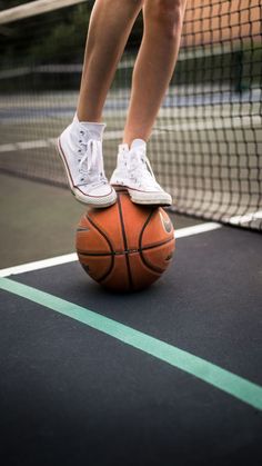 a person is standing on top of a basketball in the middle of a tennis court