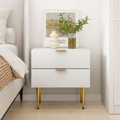 a white nightstand sitting next to a bed with a plant on it's side