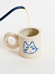 a cup with a cat drawn on it is being poured into the cup by a blue handle