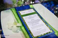 a blue and green wedding menu on a white plate with a flower in the center