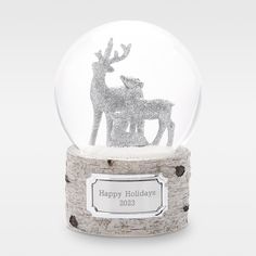 a snow globe with silver glitter reindeers on it's base and the inscription happy holidays