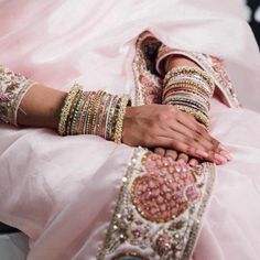 a woman in a pink wedding dress with her hands on her chest and bracelets around her arm