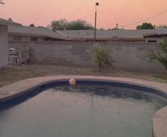 an empty swimming pool in the middle of a backyard with a fence and house behind it