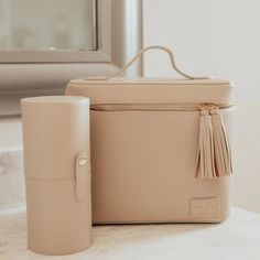 Pictured is a rectangle nude bag that includes an all around zipper with tassel pulls and a top handle. This picture includes a nude cylinder brush holder and is all pictured on a off white background. Circle E Candles, Brush Holders, Athleisure Shoes, Beauty Blenders, A Place For Everything, Tyler Candles, Bag Obsession, Travel Games, Travel Set