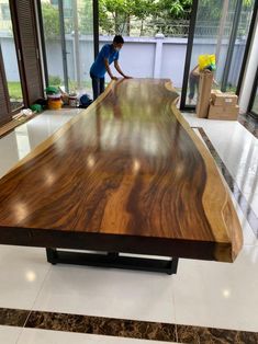 a man working on a large wooden table in the middle of a room with lots of windows