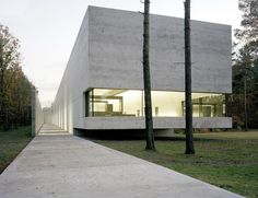 a concrete building with trees in the foreground and grass on the ground next to it