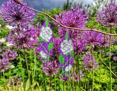 purple flowers with green and white bead designs hanging from it's stems in front of a cloudy sky