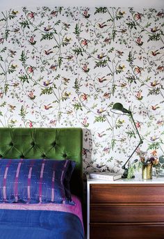 a bedroom with floral wallpaper and green headboard, blue bedding and purple bedspread