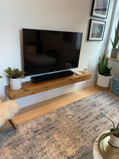 a flat screen tv sitting on top of a wooden shelf in a living room next to a window