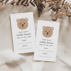 two tags with teddy bears on them sitting next to some pine cones and branches in the background