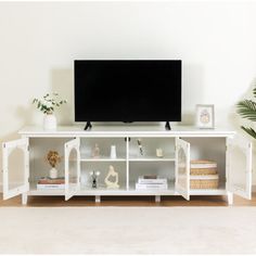 a flat screen tv sitting on top of a white entertainment center next to a potted plant