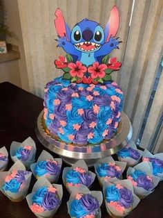 a blue and purple cake sitting on top of a table next to cupcakes