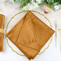 a place setting with gold napkins and flowers