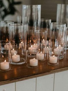 candles are lined up on a table with clear glass vases in the middle and one candle is lit