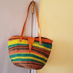 a multicolored straw bag hanging on a door handle with leather handles and straps