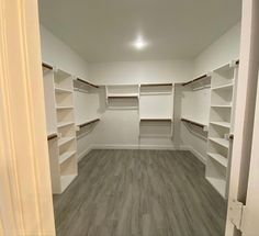 an empty walk in closet with white shelving and wood flooring on the walls