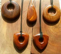 four wooden necklaces with leather cord hanging from them on a piece of plywood